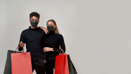 Young couple wearing black clothes and protective masks looking at camera, holding bunch of paper...