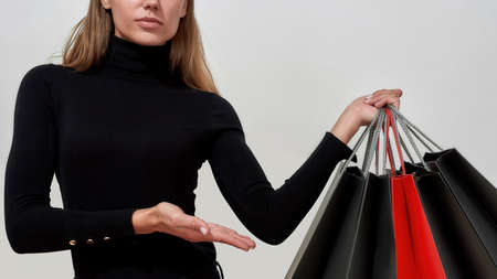 Cropped shot of young caucasian woman wearing black clothes showing bunch of shopping bags while posing isolated over light gray backgroundの写真素材