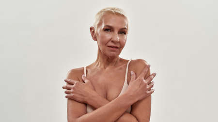 Love your body. Portrait of attractive caucasian mature woman in underwear hugging herself while...