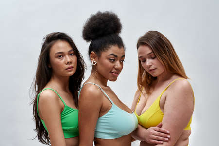 Studio portrait of three multiethnic young women in colorful underwear posing together isolated over...