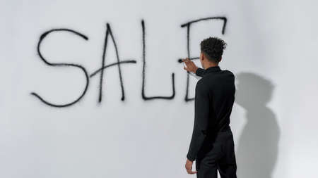 Rear view of young man writing inscription sale on wallの写真素材