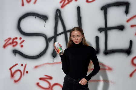 Young woman standing near wall with lettering sale