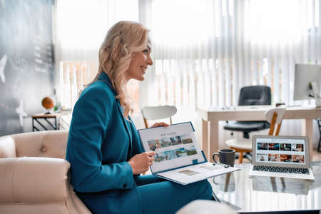 Beautiful female travel agent talking to her clients, showing catalog with tours while sitting in...