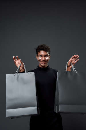Portrait of cheerful young guy holding paper bagsの写真素材