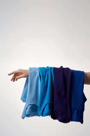 Basic T-shirts of different colors on female hand against grey backgroundの写真素材