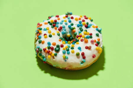 Yummy yummy. Close up shot of delicious round glazed donut with colorful sprinkles on green...