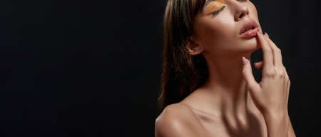 Cropped portrait of feminine brunette woman with pouty lips and bright orange makeup posing isolated over black backgroundの写真素材