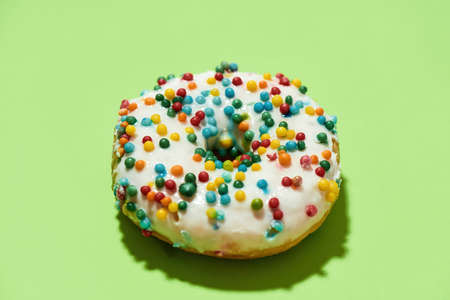 Mmm, so delicious. Close up of freshly baked round glazed donut with colorful sprinkles on green backgroundの写真素材