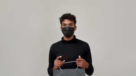 Young man in mask holding paper packet and bank cardの写真素材