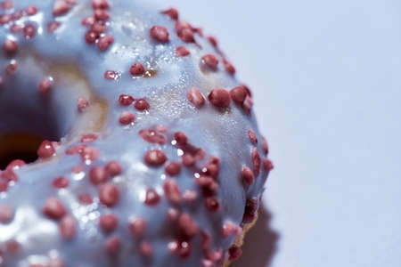 Sugar addiction. Close up shot of a freshly baked delicious donut with sprinkles and sugar glaze isolated on purple backgroundの写真素材