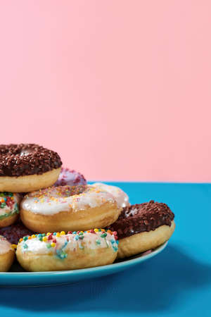 Life is sweet. Cropped shot of various colourful round glazed donuts with sprinkles on the plate over blue and pink backgroundの写真素材