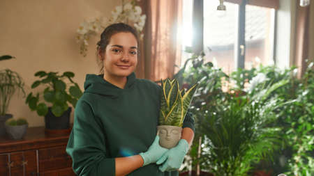Smiling young woman wearing gloves looking at camera and holding a potted plantの写真素材