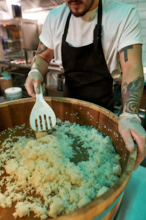 Cropped shot of male chef cook mixing, making sushi rice in a wooden barrel in the kitchen of Japanese restaurantの写真素材