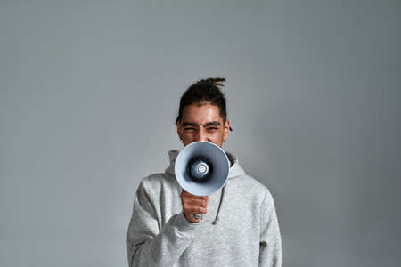 Young gypsy man with loudspeaker on light background