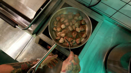 Top view of male cook stir frying pork or beef meat in wok pan while cooking in commercial kitchenの写真素材
