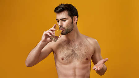 Young man with a naked torso drinks pillsの写真素材