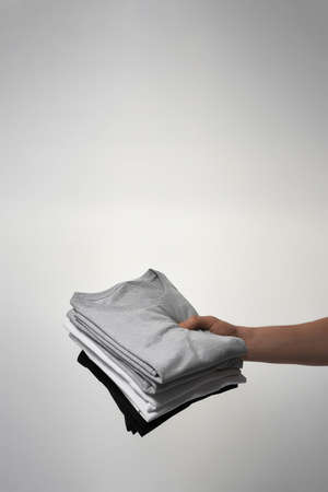 Male hand holding stack of basic mens T-shirts against gray backgroundの写真素材