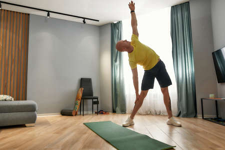 Full length shot of male coach having fitness training, working out in living room at home on a daytimeの写真素材