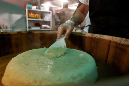 Close up of hand of male chef cook preparing sushi rice in a wooden barrel in the kitchen of...