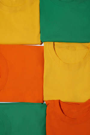 Closeup of folded colorful yellow, orange and green cotton t shirts. Flat lay tees templateの写真素材