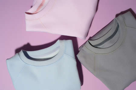 Closeup shot of three folded pastel pink, blue and gray sweatshirts isolated on pale purple backgroundの写真素材
