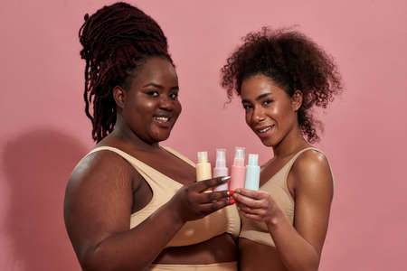 Two young afro female friends holding bottles of care productの写真素材