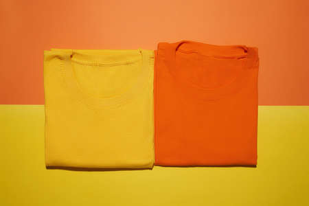 Two folded yellow and orange cotton t shirts isolated on creative colorful background. Flat lay tees templateの写真素材