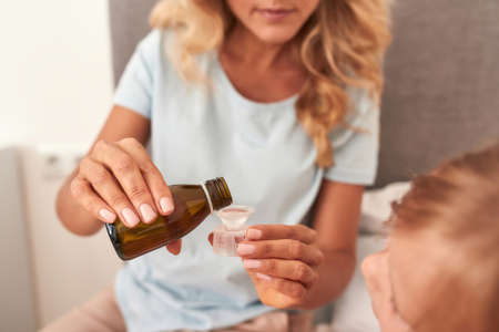 Mother gives cough syrup to her ill daughterの写真素材