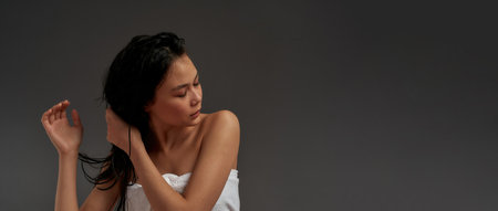 Young beautiful asian woman tousled her hair with hands in bath towel turned half-faceの写真素材