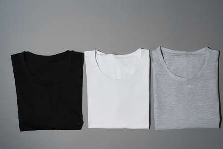 Top view of three monochrome black, white and gray cotton t shirts lying in a row. Flat lay tees...