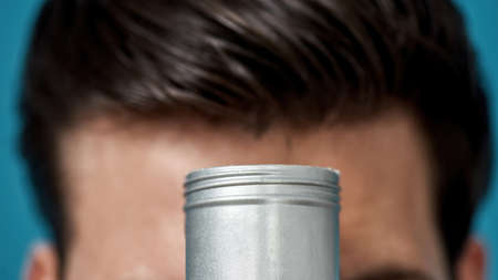 Closeup shot of silver jar with gel or cream hair styling product with male head in the background