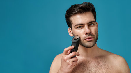 Beauty portrait of handsome young man using electric shaver isolated over blue backgroundの写真素材