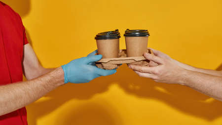 Hands of courier in gloves giving cups to customerの写真素材