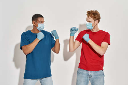 Multiracial young couriers in gloves and masks boxing
