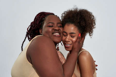 Portrait of happy friends, african american women in underwear with different body size smiling, hugging each other while posing together isolated over gray backgroundの写真素材