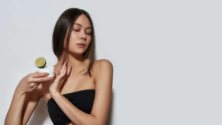 Sensual asian woman holding citrus and cosmetology creamの写真素材