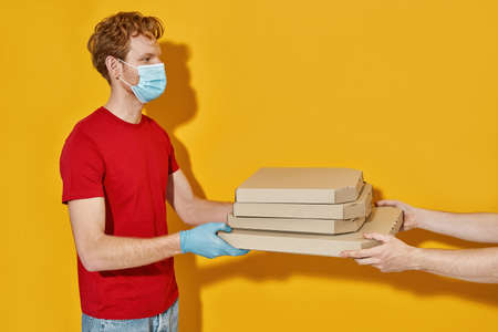 Courier in protective mask giving pizza boxes to customerの写真素材