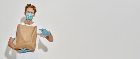 Picture of a young redhead courier holding paper bag and pointing at it with a fingerの写真素材