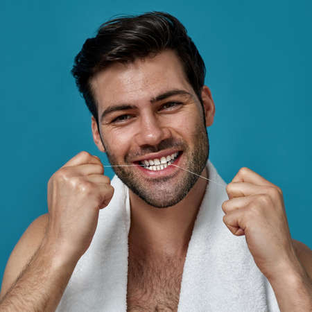Beauty portrait of joyful brunette guy looking at camera while cleaning his teeth using dental floss...
