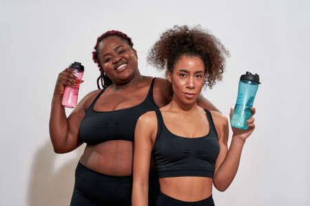 Two afro women clothed in sport black tops and holding bottlesの写真素材