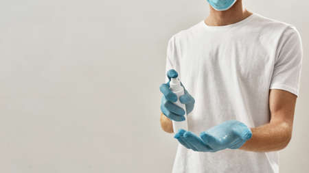 Cropped photo of a young man in gloves and mask using sanitizer