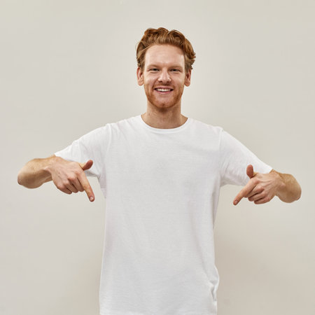 Young redhead man smiles and points with fingers downの写真素材