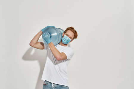 Young, redhead deliveryman holds giant bottle with both hands on his shoulderの写真素材