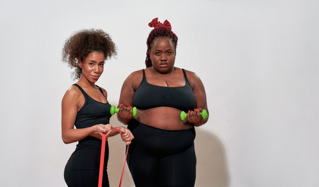 Picture of two afro women holding dumbbells and skipping rope, posing sexyの写真素材
