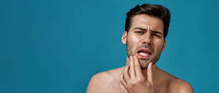 Portrait of shirtless handsome brunette guy checking his facial skin, looking at camera isolated...