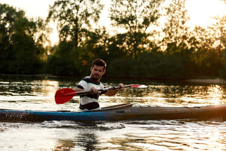 Cheerful young caucasian man having fun while kayaking on a lake surrounded by natureの写真素材