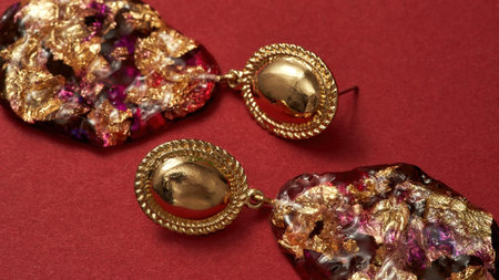 Close up shot of epoxy resin earrings with golden foil inside isolated over red backgroundの写真素材