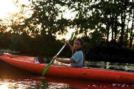 Relaxed young woman looking aside while paddling kayak on a lake surrounded by natureの写真素材