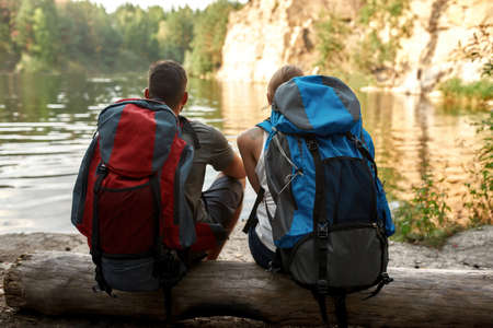 Rear view of young tourists on log near lakeの写真素材