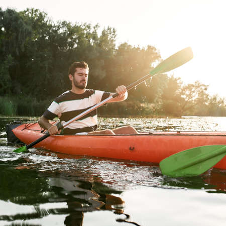 Focused young man kayaking together with his friend in a lake on a late summer afternoonの写真素材